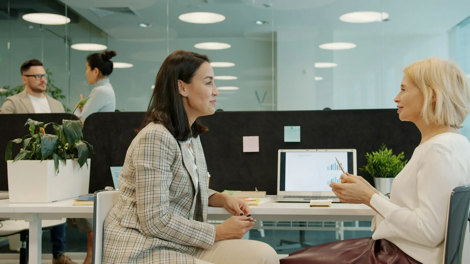 Two women talking through a project at a desk in a bright office