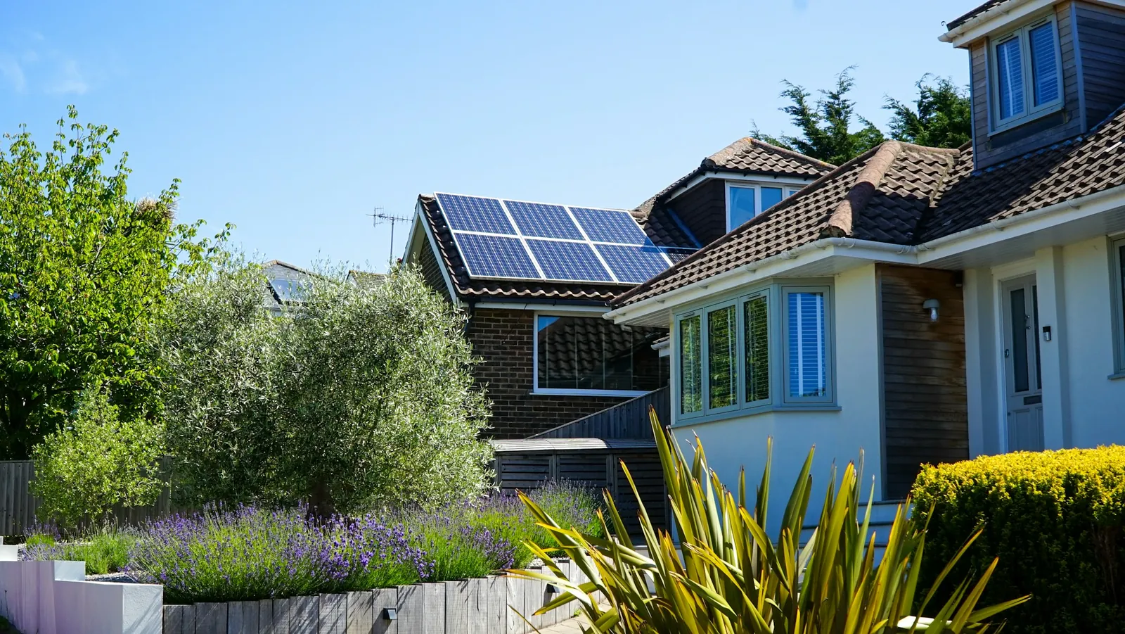 A house with solar panels on a tiled roof beside a garden