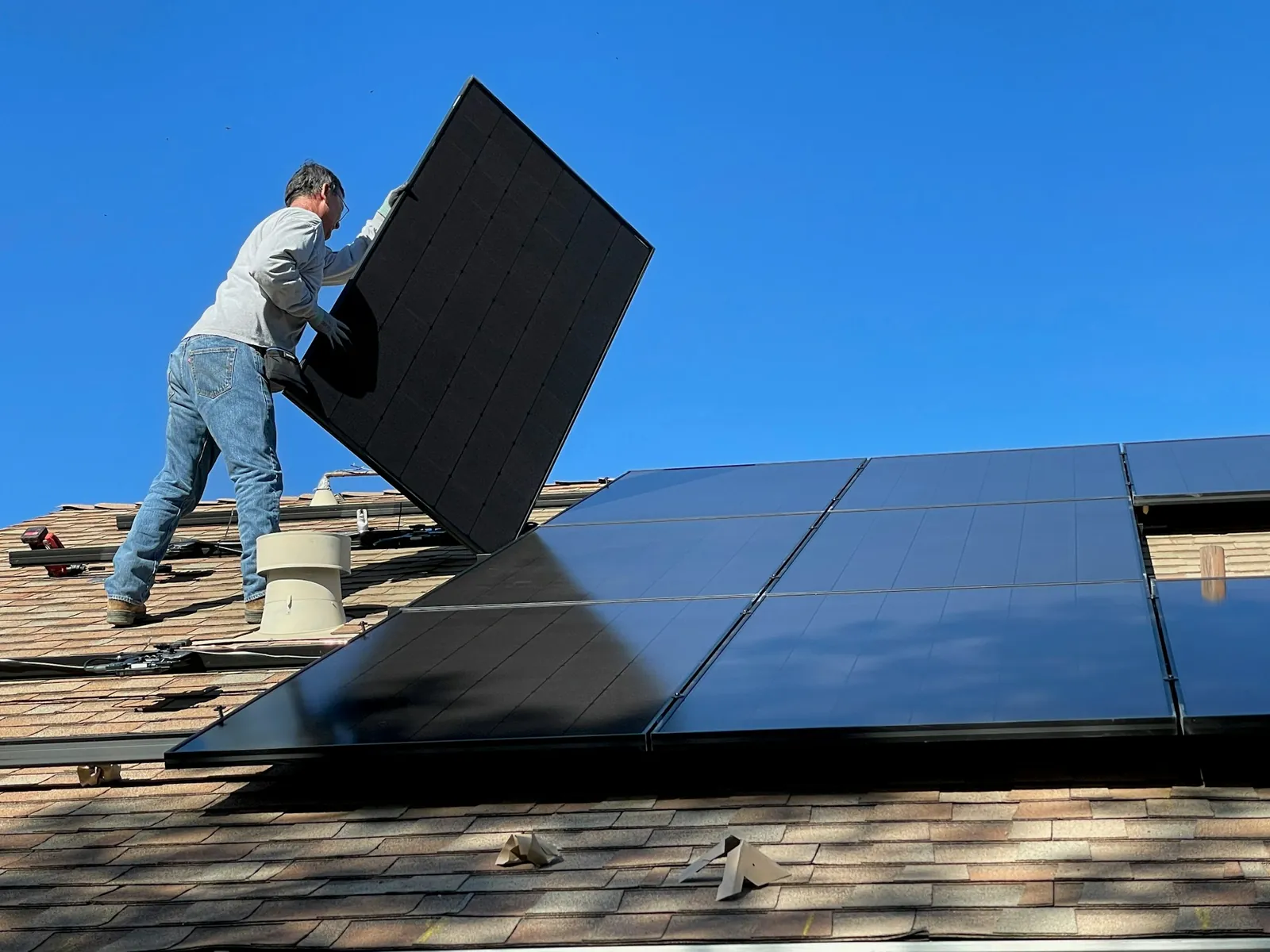 An installer lifting a black solar panel into place on a tiled roof